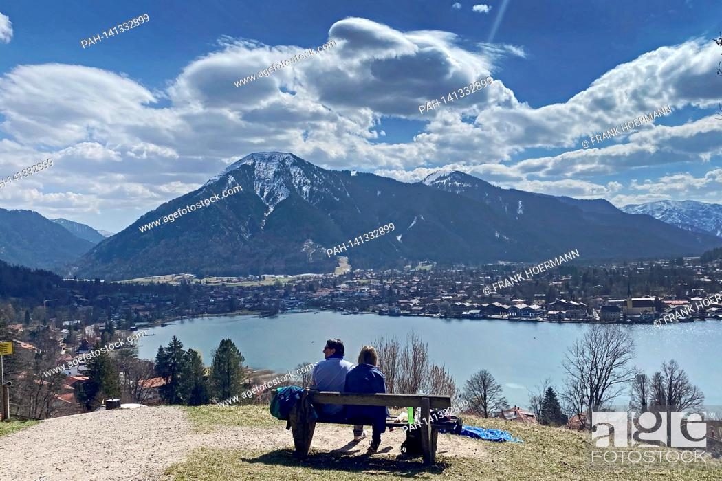 Stock Photo: Couple takes a rest on a bench. Hikers on the Hoehenweg over the Tegernsee with a view of Rottach Egern on April 1st, 2021.