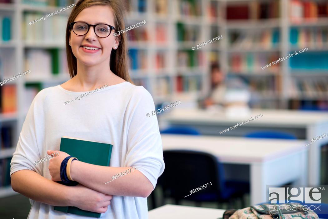 Stock Photo: portrait of happy smilling female student girl in school library bholding book.