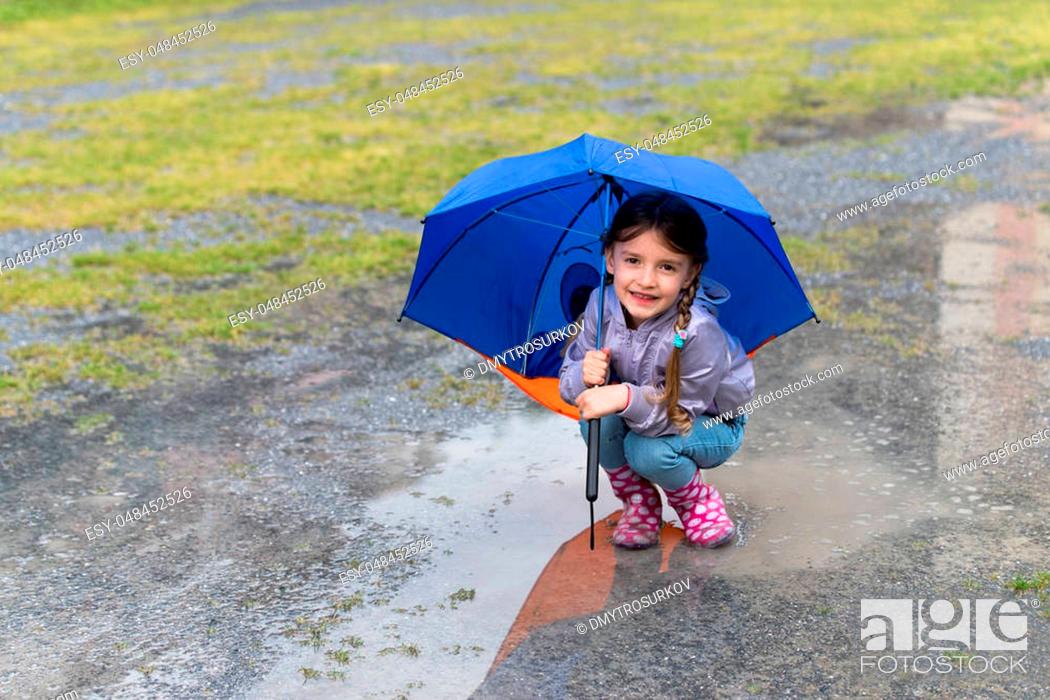 Stock Photo: Little girl playing in the rain under umbrella.