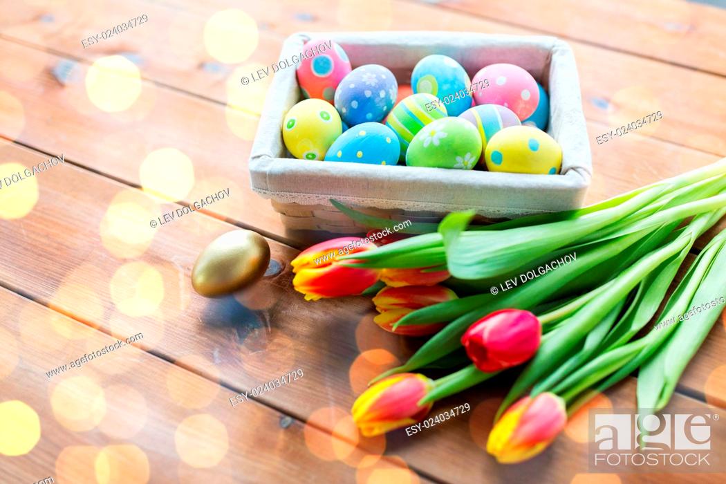 Stock Photo: easter, holidays, tradition and object concept - close up of colored easter eggs in basket and tulip flowers.
