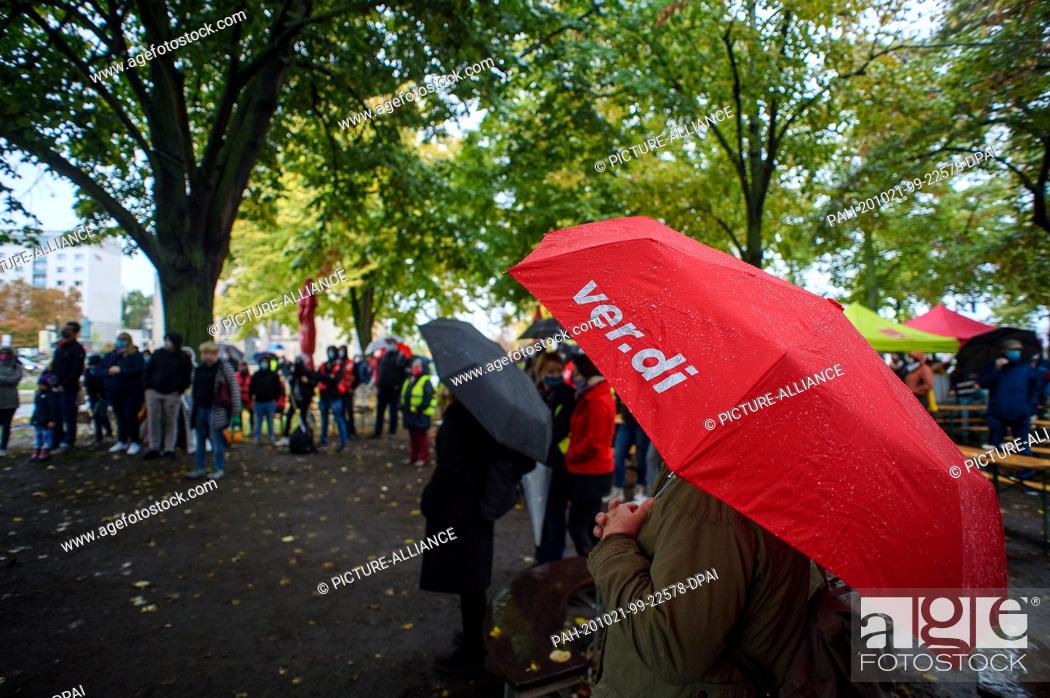 Stock Photo: 21 October 2020, Saxony-Anhalt, Magdeburg: ""Ver.di"" can be read on the red screen of a female public service worker who has come to a strike rally.