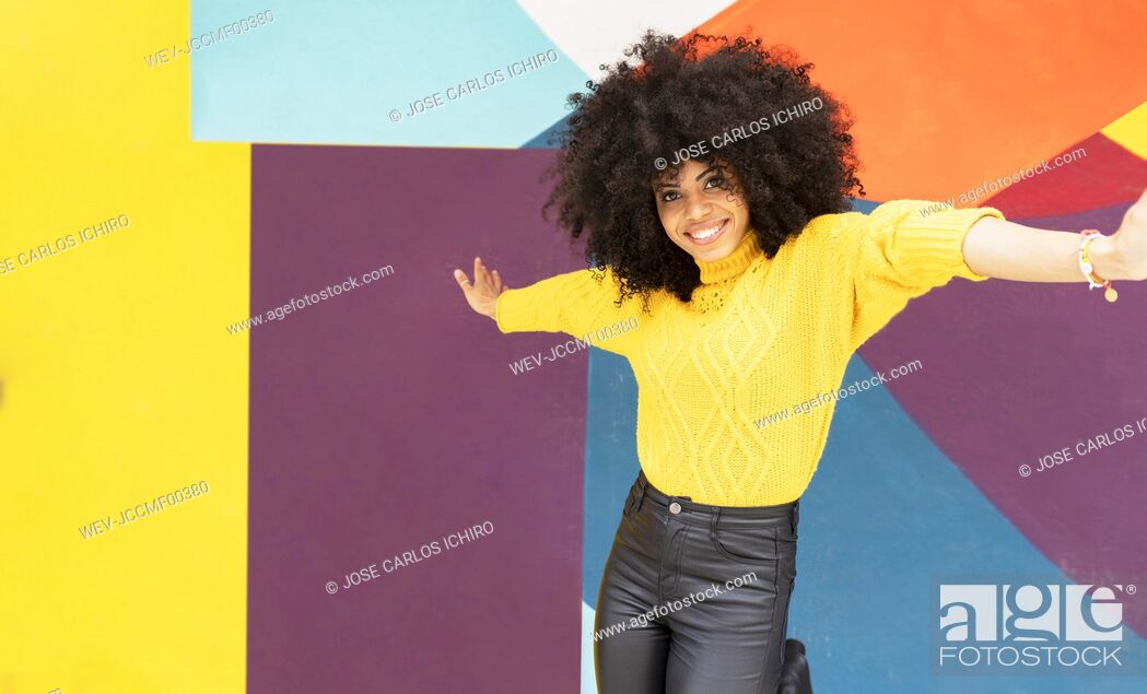 Stock Photo: Carefree woman dancing with arms outstretched against multi colored wall.