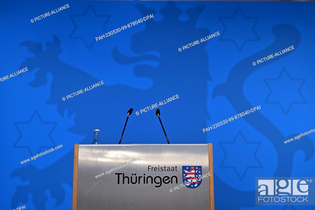 Stock Photo: 30 May 2023, Thuringia, Erfurt: The lectern with microphones and the inscription ""Free State of Thuringia"" including coat of arms in front of a blue wall with.