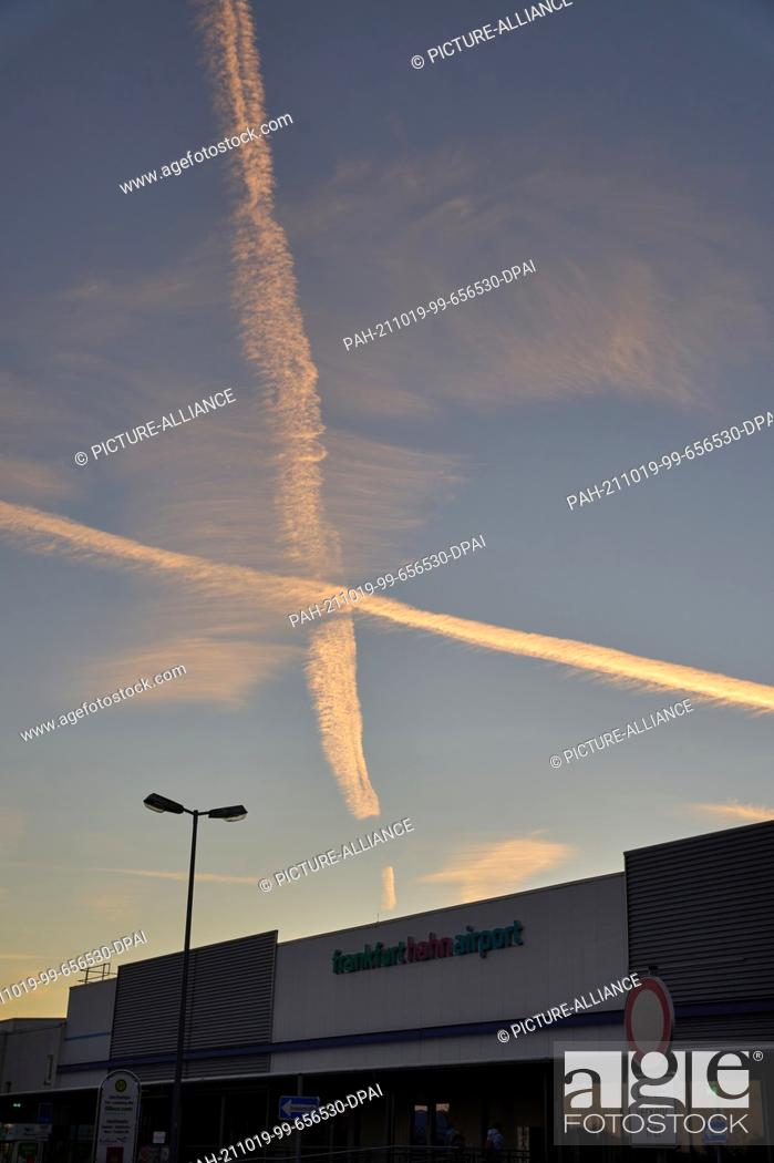 Stock Photo: 19 October 2021, Rhineland-Palatinate, Hahn: The vapour trails of two aircraft cross over the terminal of the former American military airport Hahn in Hunsrück.