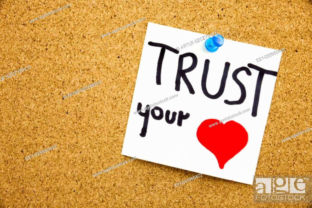 Stock Photo: Phrase TRUST YOUR HEART in black ext on a sticky note pinned to a cork notice board.