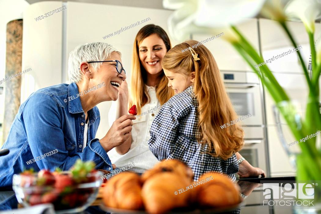 Stock Photo: Grandmother offering stawberry to granddaughter, mother watching.