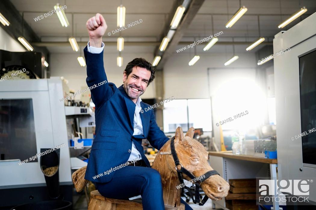 Stock Photo: Portrait of a playful businessman on wooden rocking horse in a factory.