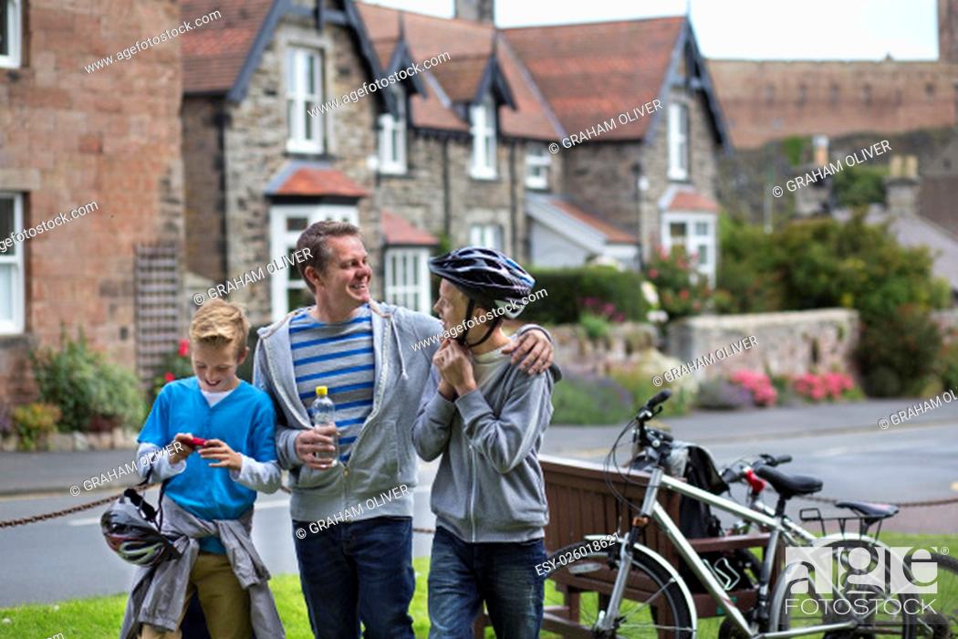 Stock Photo: Father and Sons stopping in a village in the middle of their bike ride to take a drink. They are wearing casual clothing and smiling.