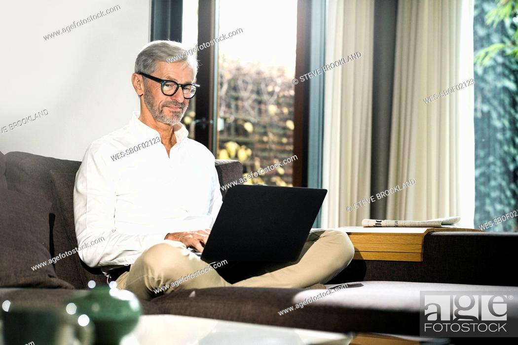 Stock Photo: Senior man with grey hair in modern design living room working on laptop in home office.