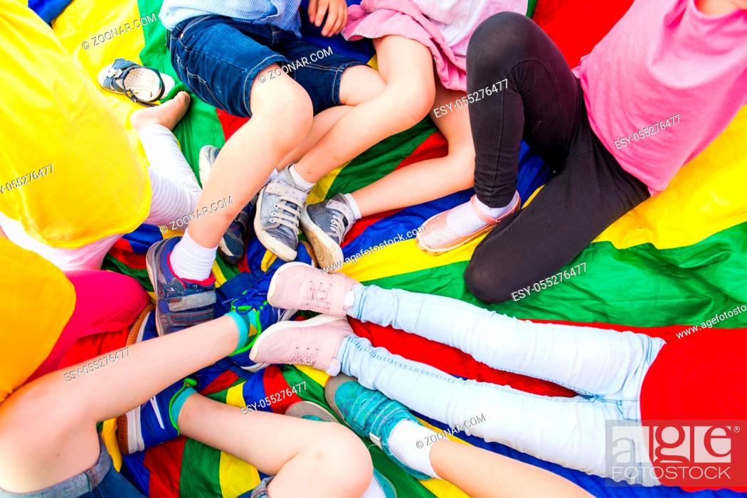 Stock Photo: Close view of children's legs laying in a circle on a rainbow parachute. After school outdoor activities.