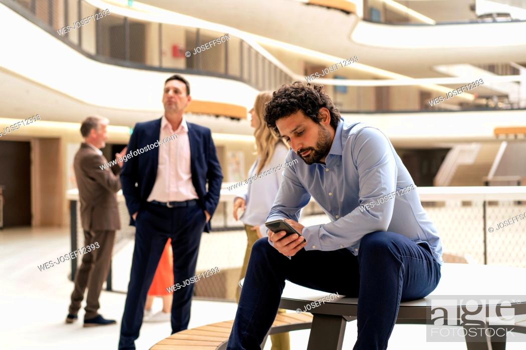 Imagen: Businessman using mobile phone with colleagues in background at office.