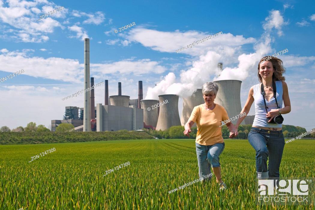 Stock Photo: 2 Frauen rennen durch ein getreidefeld vor dem Kraftwerk Neurath.