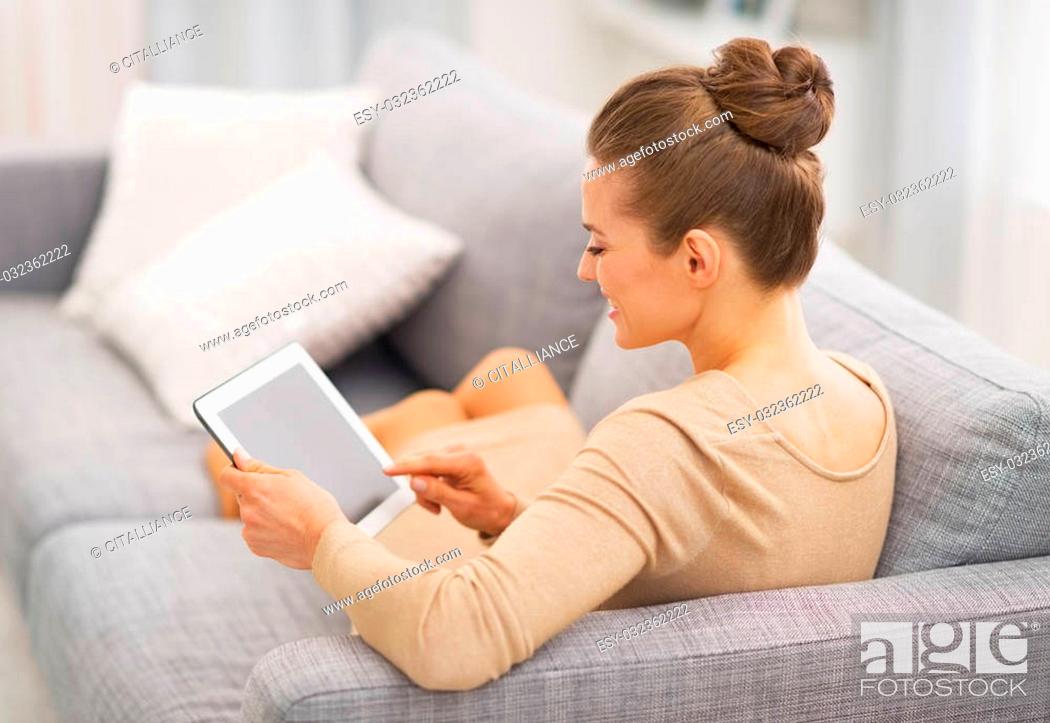Stock Photo: Young housewife sitting on couch using tablet pc . rear view.