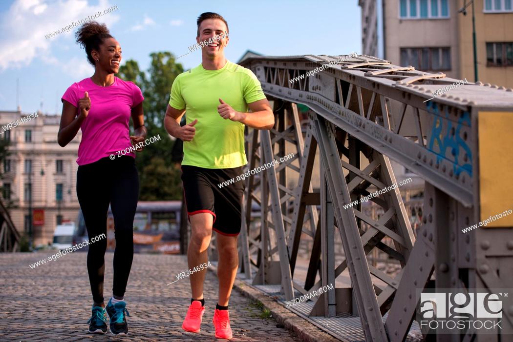 Stock Photo: healthy young multiethnic couple jogging across the bridge in the city at early morning with sunrise in background.