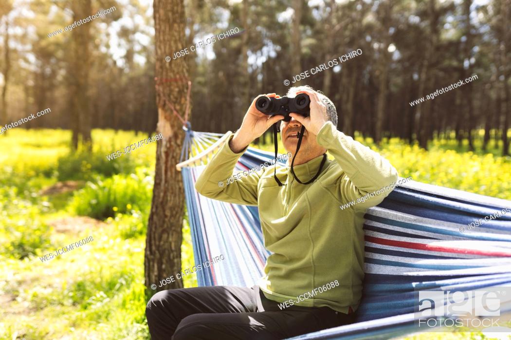 Stock Photo: Man looking through binoculars sitting in hammock on sunny day.