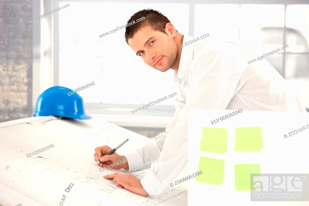 Stock Photo: Handsome young engineer drawing plans in bright office.