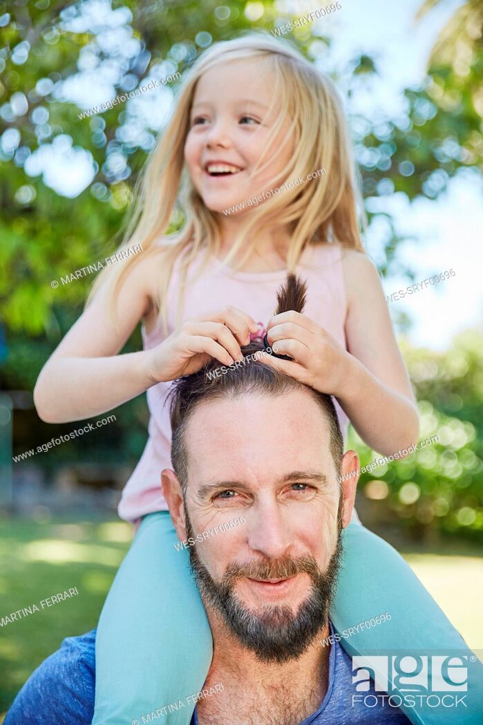 Stock Photo: Happy girl sitting on father's shoulders doing his hair.