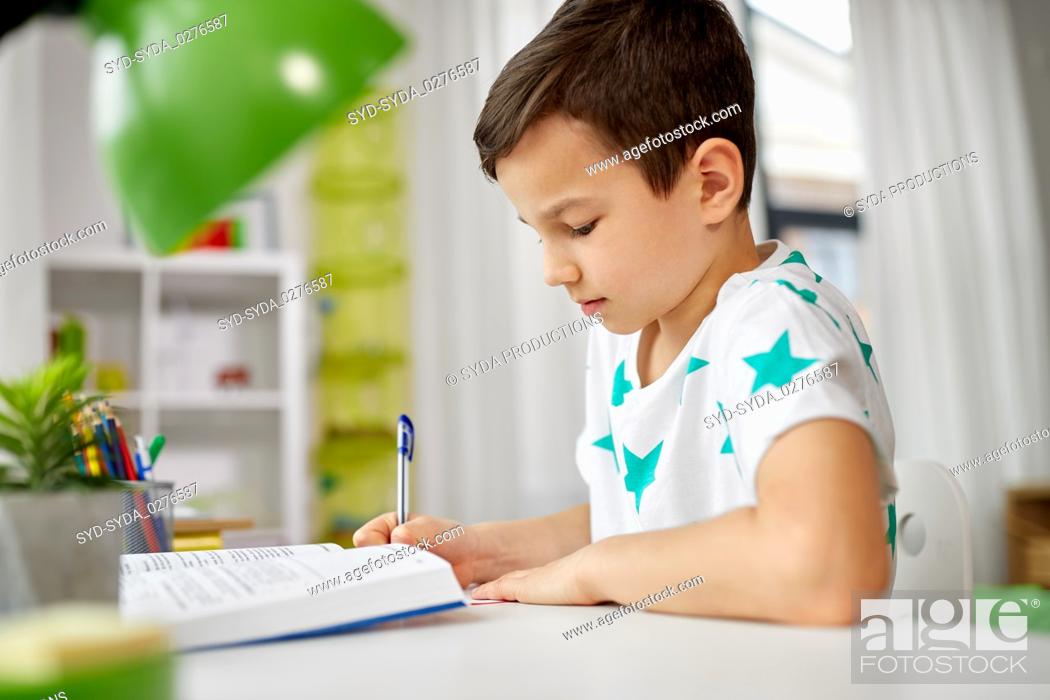 Stock Photo: student boy with book writing to notebook at home.