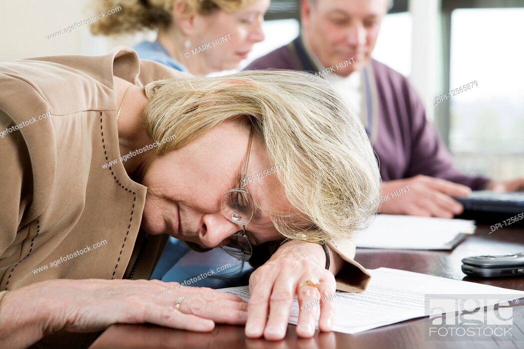Stock Photo: Mature woman sleeping on the desk with mature couple sitting in the background.