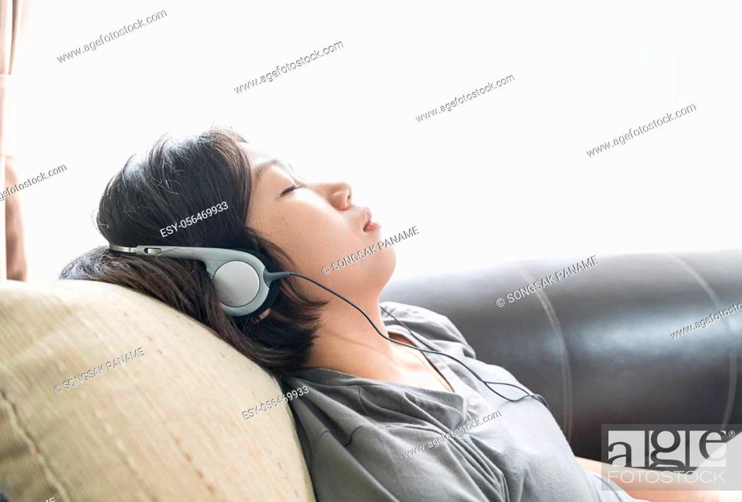 Stock Photo: Close up beautiful young asian woman short hair listening music on the couch at home.