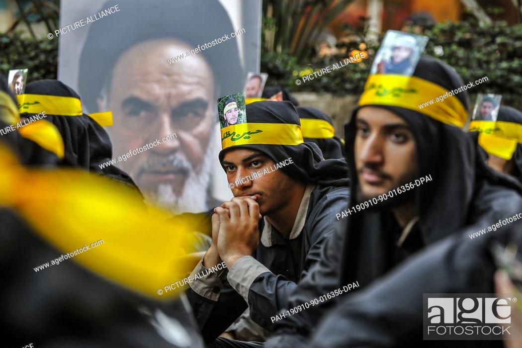 Stock Photo: 10 September 2019, Lebanon, Beirut: Supporters of Hezbollah, the Shia pro-Iranian political party and militant group, sit next to a poster of Ayatollah Khomeini.