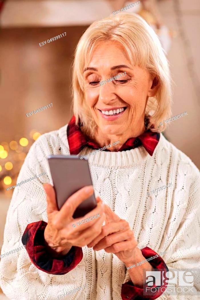 Stock Photo: Want to congratulate everybody. Pretty blonde keeping smile on her face and holding telephone in right hand while typing message.