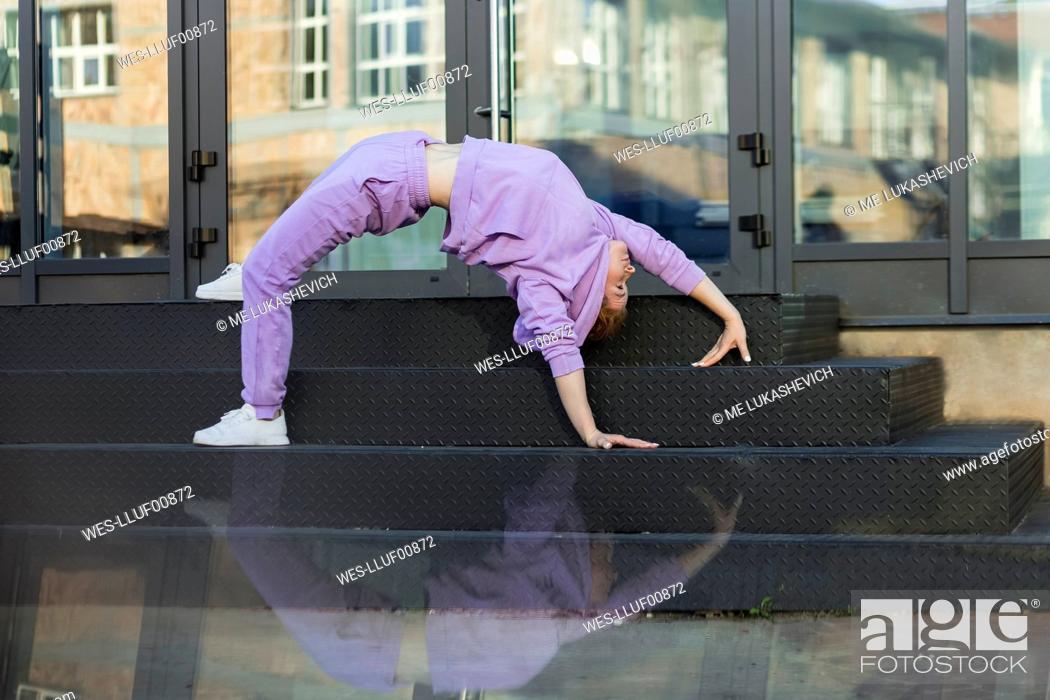Stock Photo: Woman exercising bridge position on staircase in front of glass door.