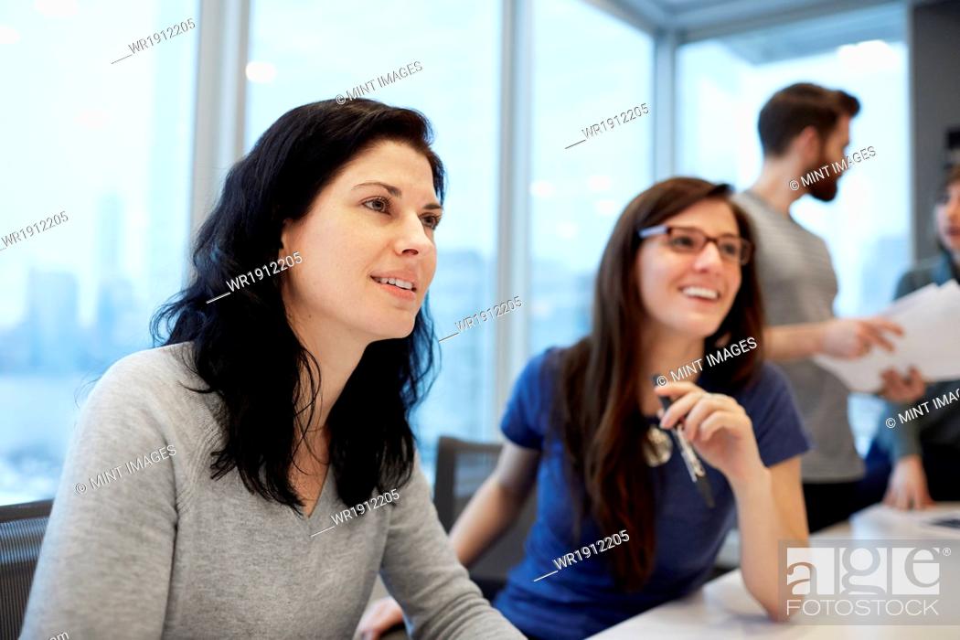 Stock Photo: Two businesswomen, women seated at a desk talking animatedly.