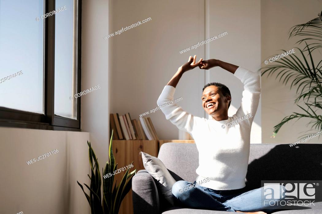 Stock Photo: Laughing woman sitting on couch at home stretching her arms.