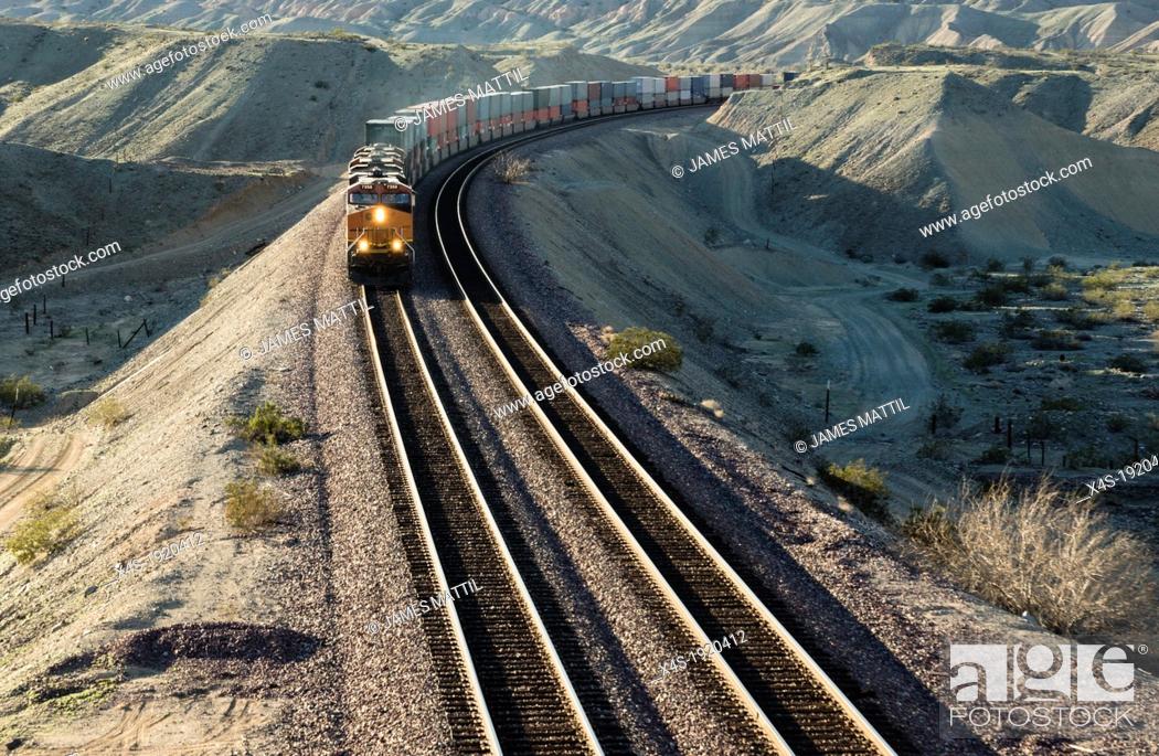 Stock Photo: A frieght train rounds a bend in the aride California desert in late afternoon.