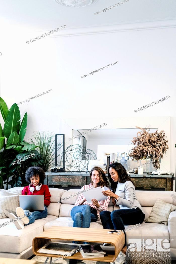 Stock Photo: Three women with laptop and documents sitting on couch.