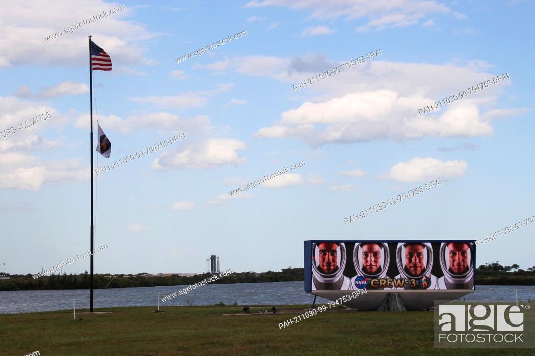 Stock Photo: 29 October 2021, US, Cape Canaveral: A US flag flies next to a video screen with the faces of the four astronauts of Crew-3 (l-r): Raja Chari, Kayla Barron.