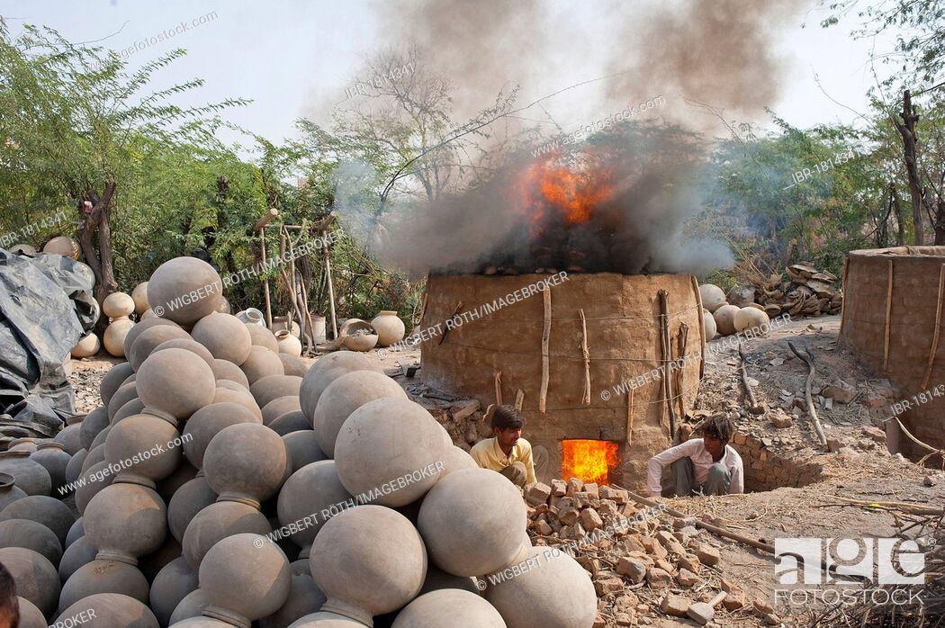 Stock Photo: A clay kiln for firing clay water jugs, two potters puting more firewood on the kiln, in front stacked finished water jugs, Bishnoi, Jodhpur, Rajasthan, India.