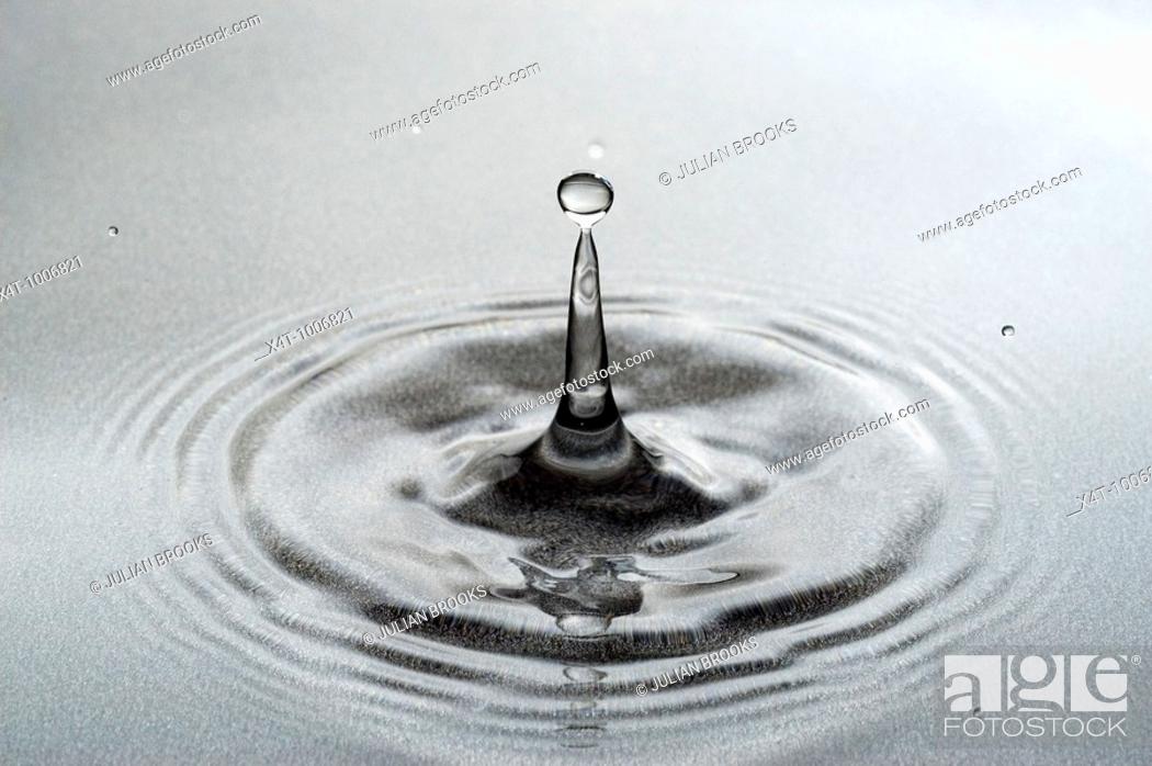 Stock Photo: A drop of water falling into a pool forming a classic column with drops  Close up.