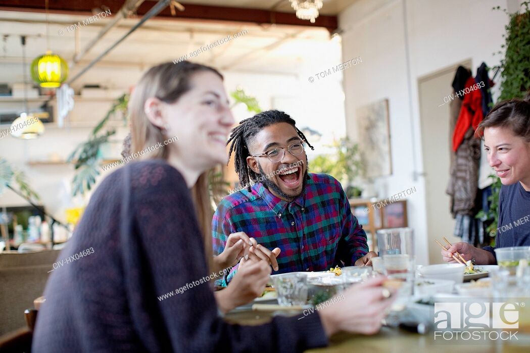 Stock Photo: Happy young adult roommates eating take out food at kitchen table in apartment.