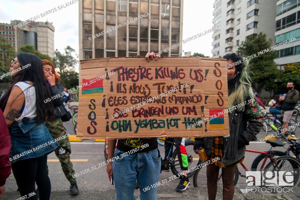 Stock Photo: A demonstrator holds a sign alusive to S.O.S Colombia in several languajes that read ""They are killing us"" in Bogota, Colombia on May 7 2021 after peaceful.