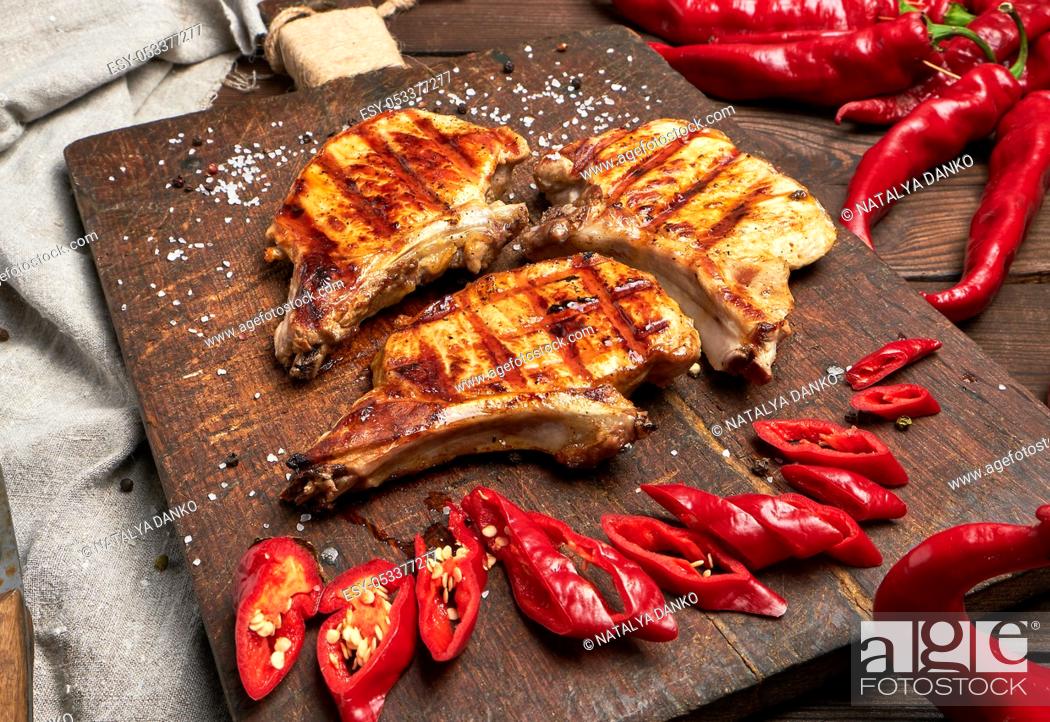 Stock Photo: pork fried steak on the rib lies on a vintage brown wooden board, next to fresh red chili peppers, top view.