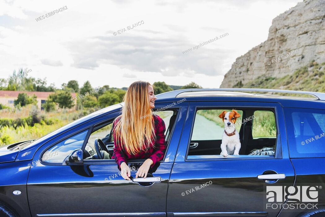 Stock Photo: Happy young blond woman and pet dog at car's windows.