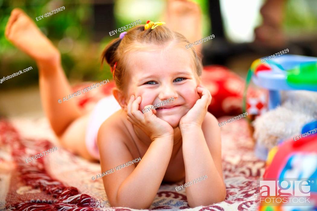 Photo de stock: Happy smiling baby girl lying on a blanket outdoors. Little girl resting his head on his hands and looking into the camera. Shallow depth of field.