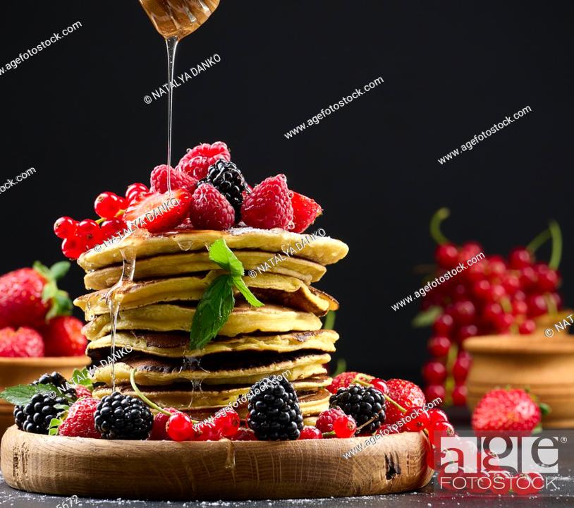 Imagen: Stack of pancakes with fresh fruit sprinkled with honey on a black background.