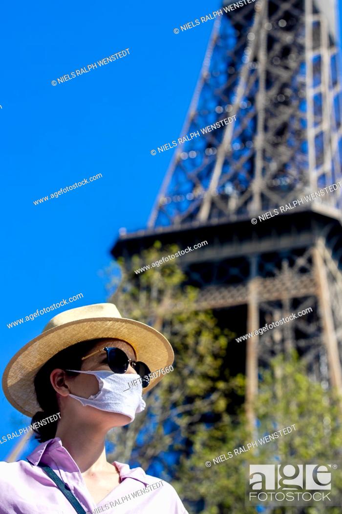 Stock Photo: PARIS - An young French woman with a mouthmask to protect her against the coronavirus, in front of the Eiffel Tower. France will extend its nationwide lockdown.