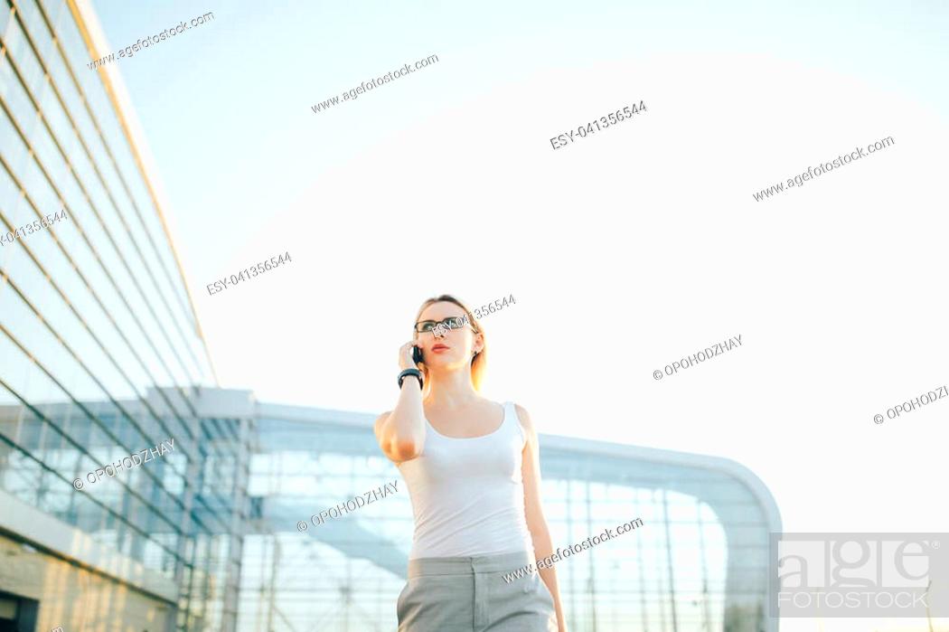 Stock Photo: Attractive business woman using a phone and clock while standing in front of windows in an office building overlooking the city.
