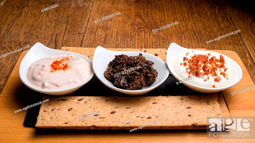 Stock Photo: Three different sauces served on a wooden table along. First sauce is made from sour cream and smoked peppers, second sauce is made from olives and smoked.