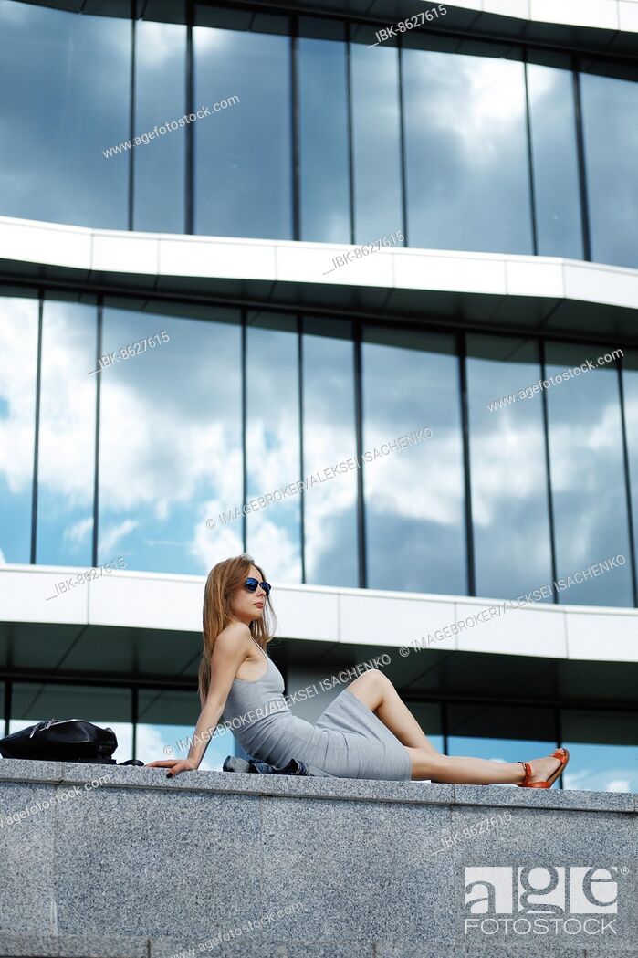 Stock Photo: Pretty girl sitting on marble surface with bent knee. Reflection of the sky in windows.