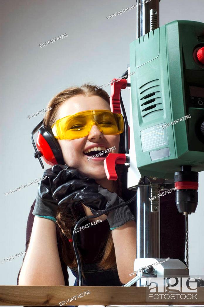 Stock Photo: beautiful female carpenter at work using vertical drilling machine.