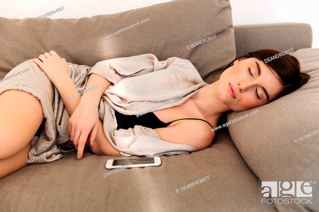 Stock Photo: Beautiful tender woman wearing housecoat resting at home and sleeping on sofa with smartphone.