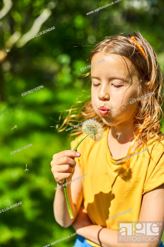 Stock Photo: Adorable little girl blowing on a dandelion on a sunny summer day, summertime vacation.