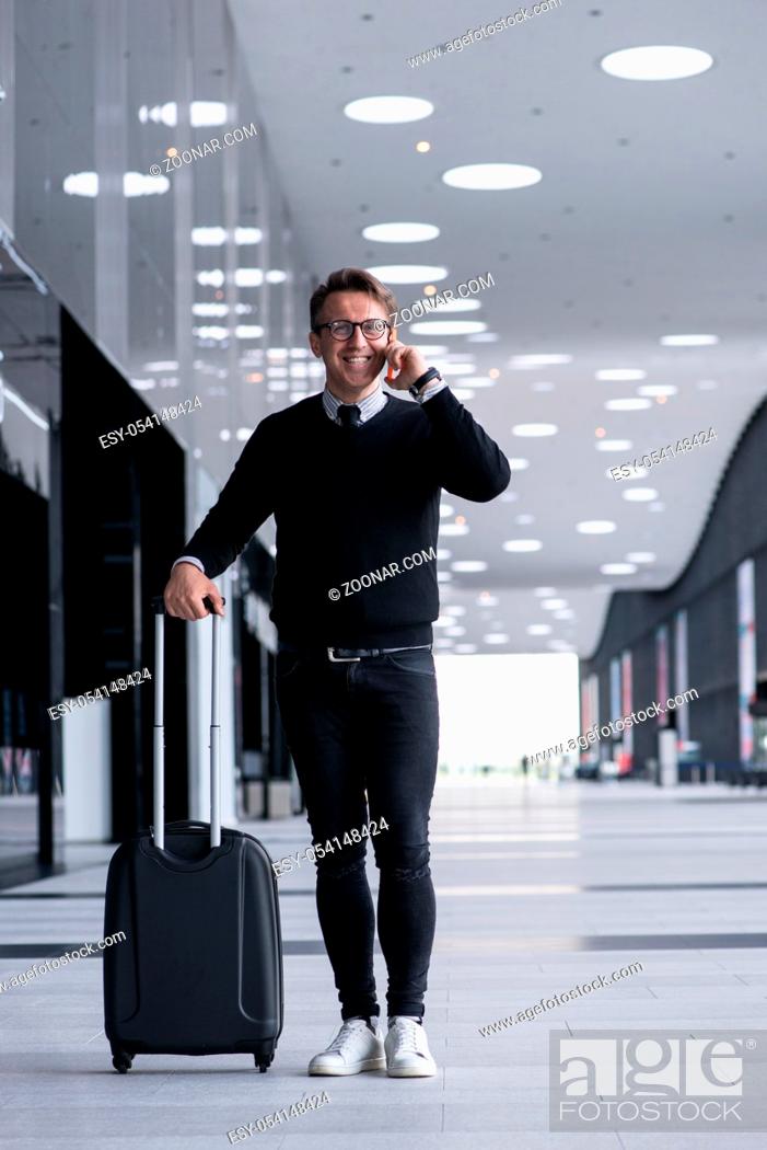 Stock Photo: Man walking with wheeled bag at airport terminal and talking on phone.