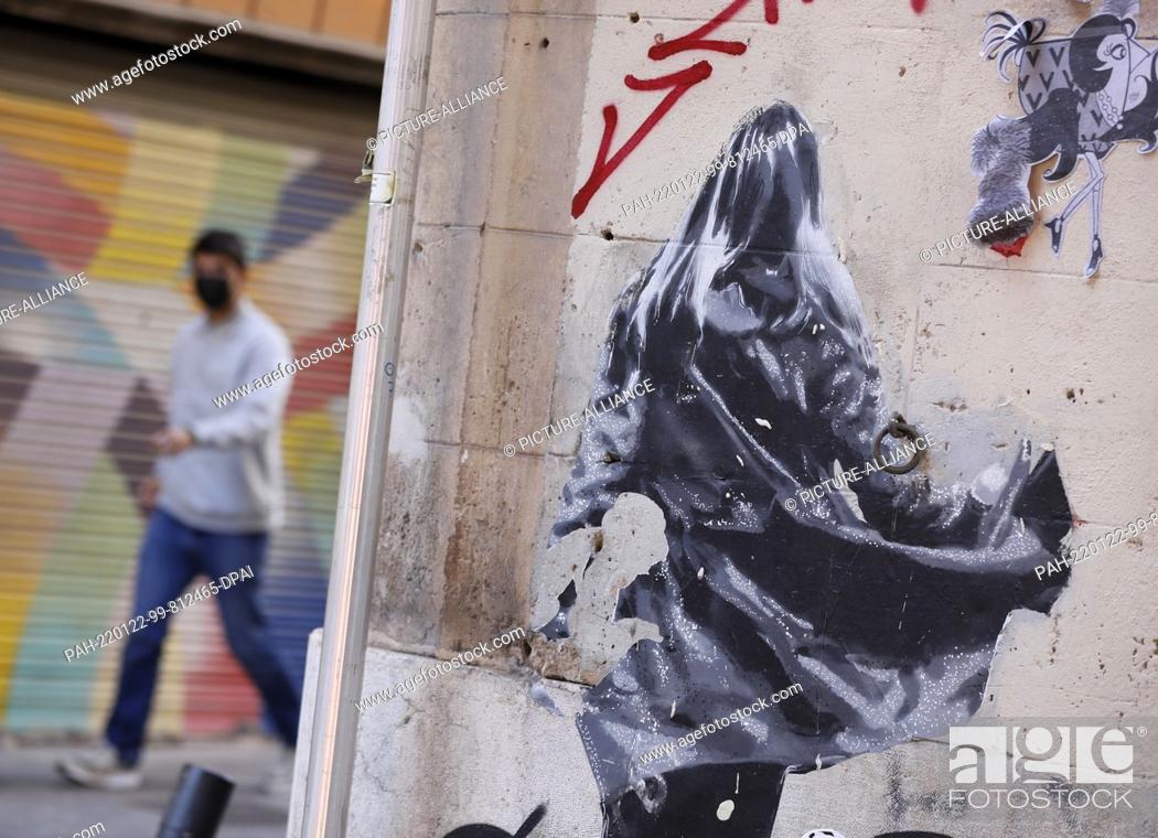 Stock Photo: 22 January 2022, Spain, Palma: A man wearing a face shield walks past graffiti in Palma. The 14-day incidence in Mallorca is currently 3239 people tested.