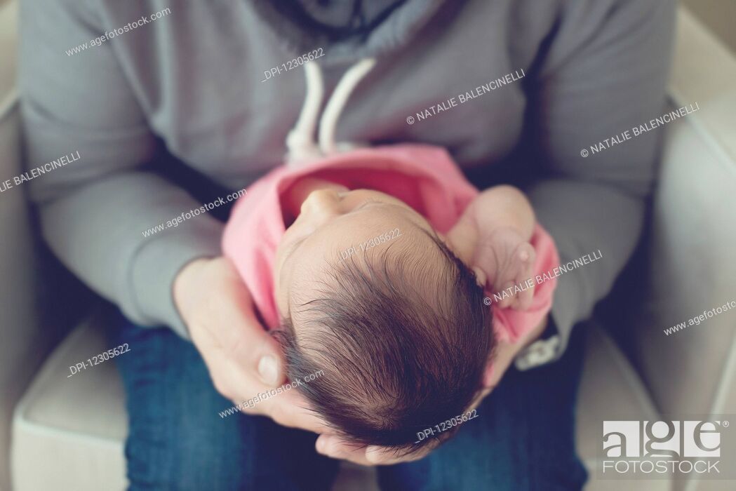 Stock Photo: An adult holding a newborn baby while sitting in a white chair; Toronto, Ontario, Canada.